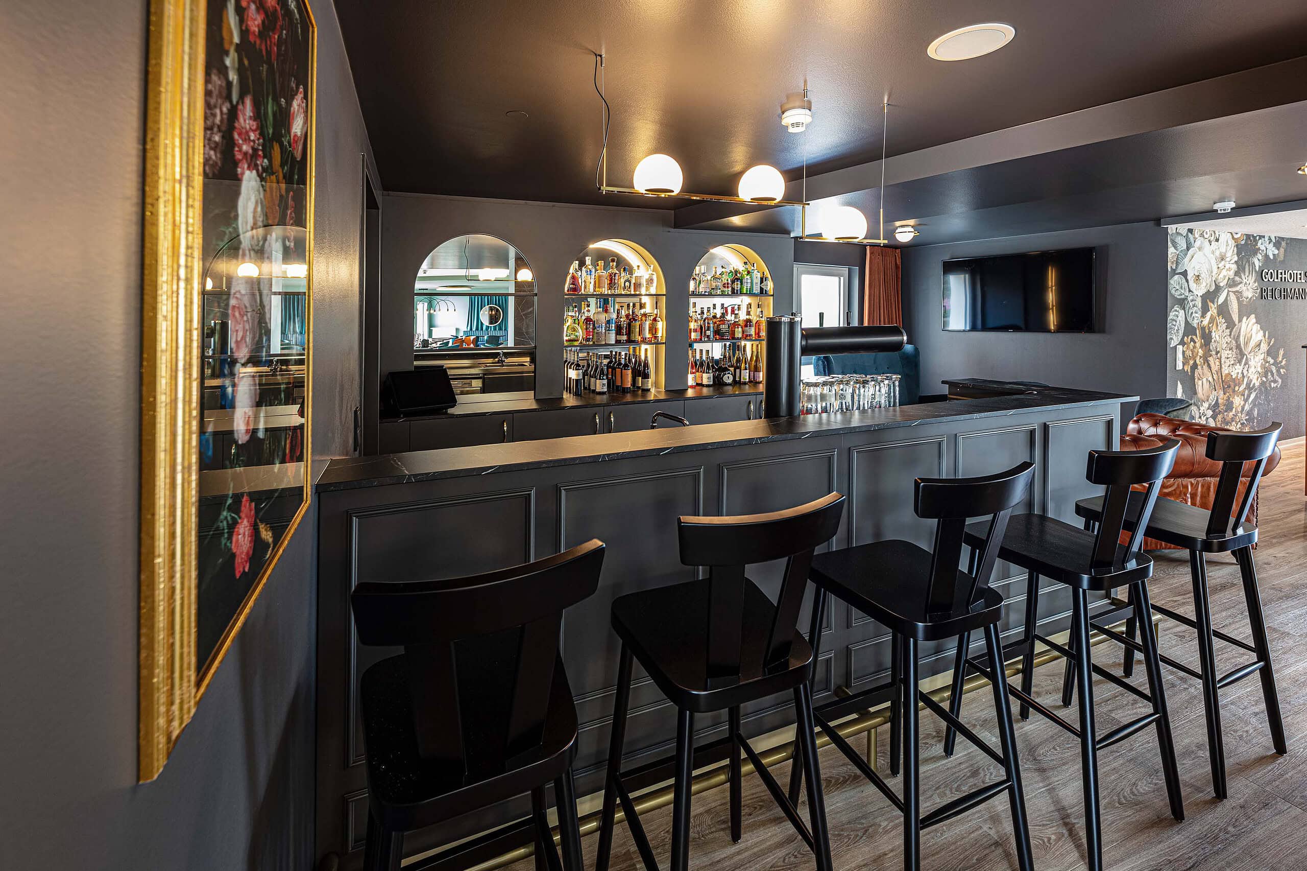 Dunkle Hotelbar mit schwarzen Barhockern, Goldrahmen und beleuchteten Regalen