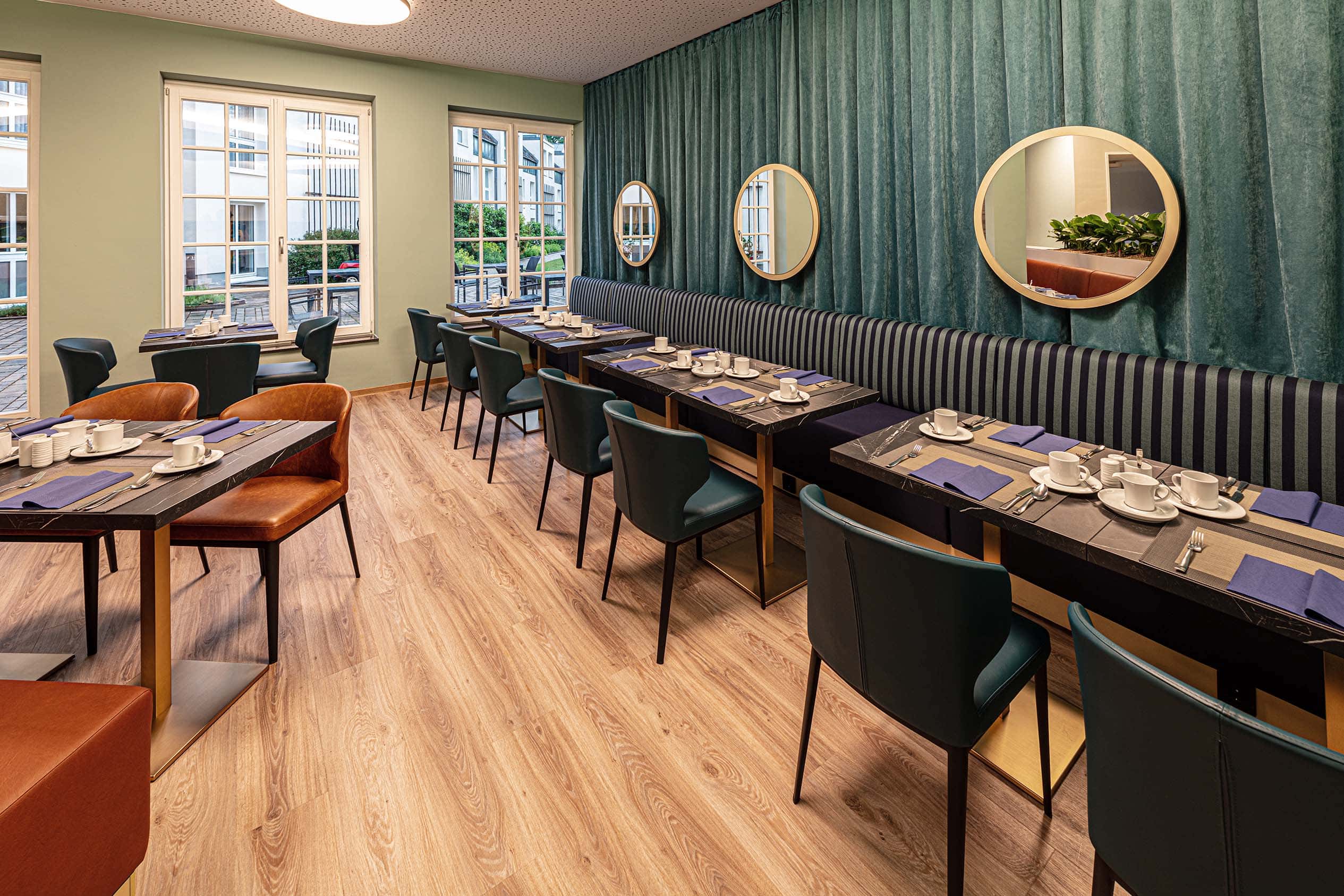 Restaurant mit grüner Wand, runden Spiegeln, Sitzbank und Lederstühlen