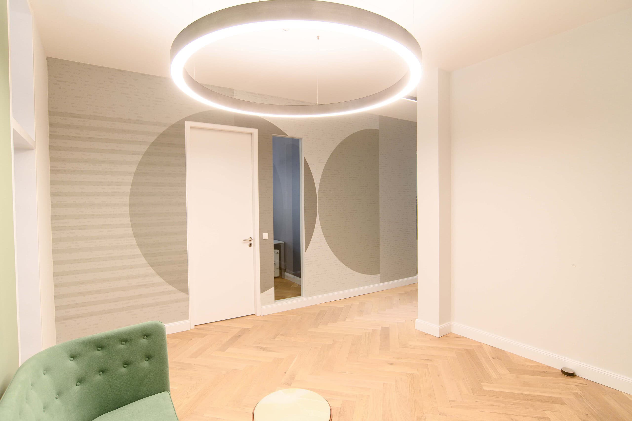 Empfangsraum mit Ringleuchte, grünem Sofa und großen Kreis-Motiven an der Wand