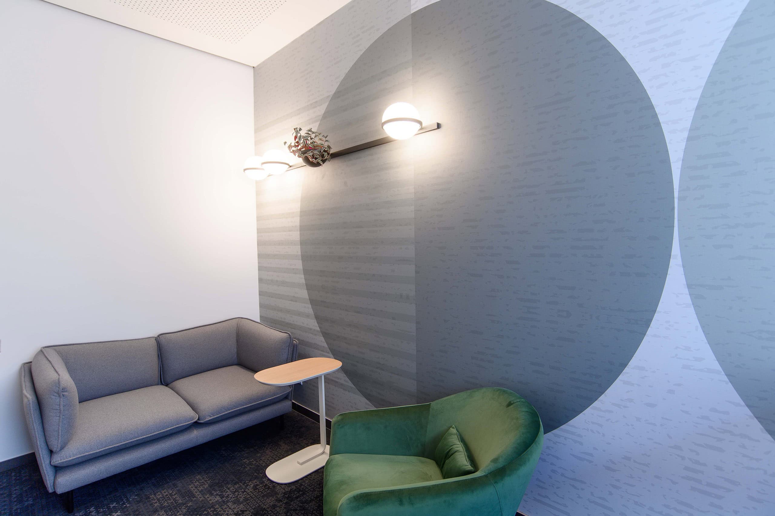Lounge mit grauem Sofa, grünem Sessel und Wandleuchte vor Kreis-Motiv