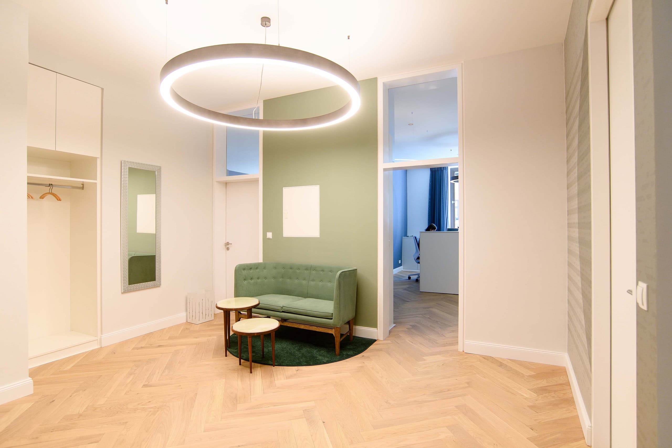 Wartebereich mit grünem Sofa, Garderobe und Ringleuchte