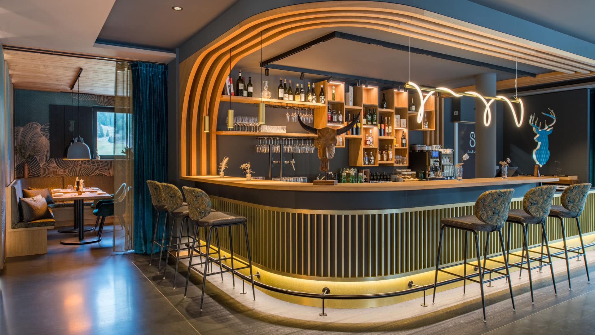 Innenarchitektur München / Innenarchitektur Federleicht - Barbereich La Soa Chalets mit geschwungenem Tresen, Holzdetails und Messingakzenten im modernen alpinen Stil