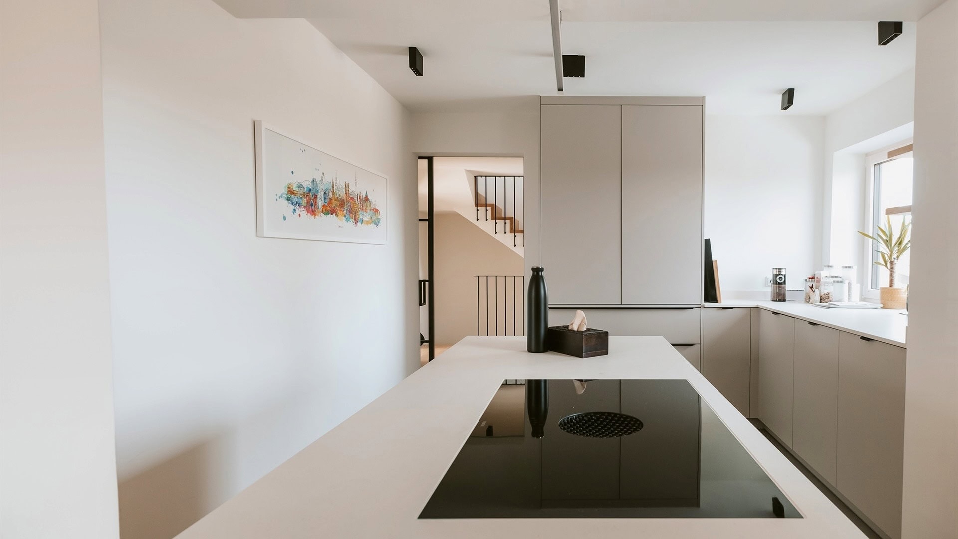 Innenarchitektur München, Büro Innenarchitektur Federleicht – Sanierung/Renovierung Reihenendhaus, moderne Küche mit Kochinsel, klaren Linien und Blick auf ein stilvolles Treppenhaus