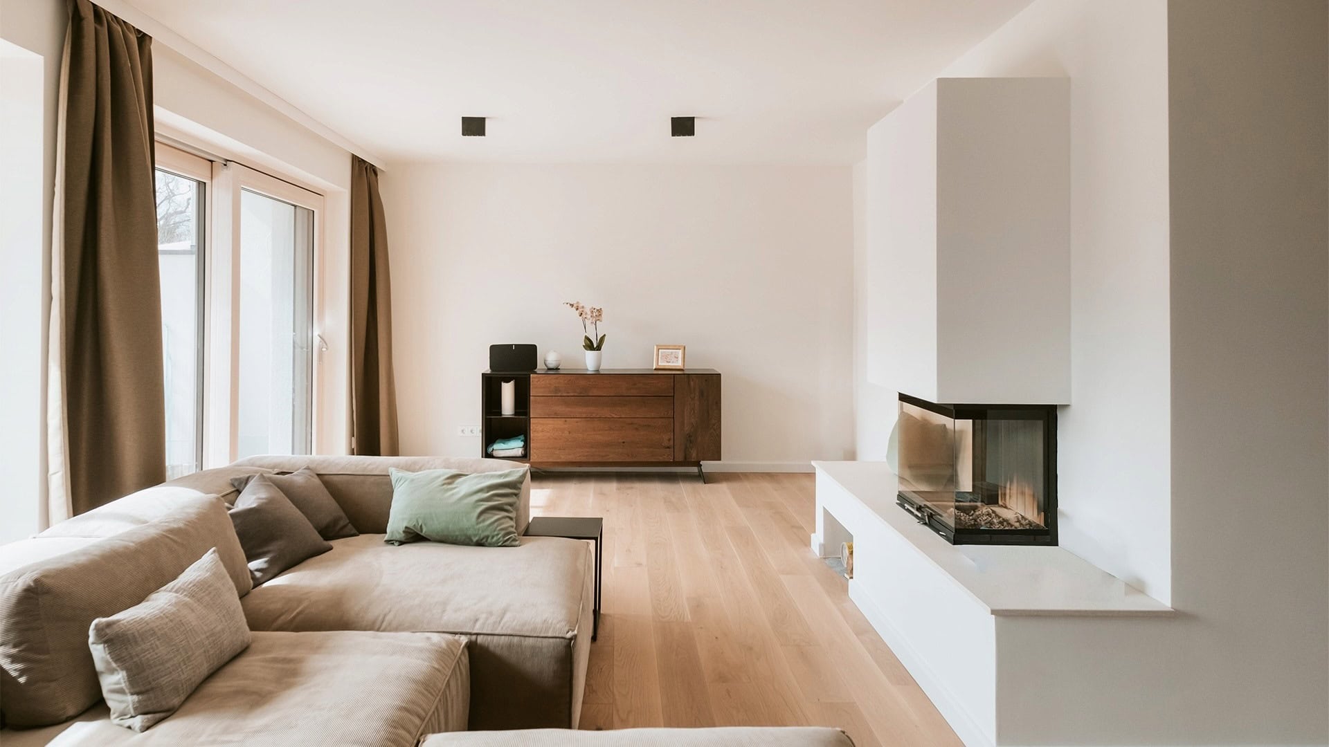 Innenarchitektur München, Büro Innenarchitektur Federleicht – Moderner Wohnbereich mit hellem Holzfußboden, gemütlichem Kamin und elegantem Sideboard
