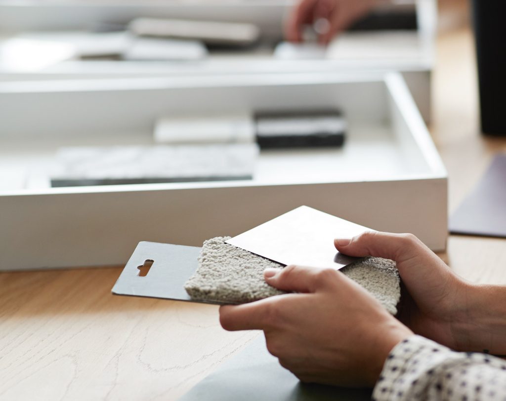 Hände halten ein Natursteinmuster über einer Box mit Materialproben