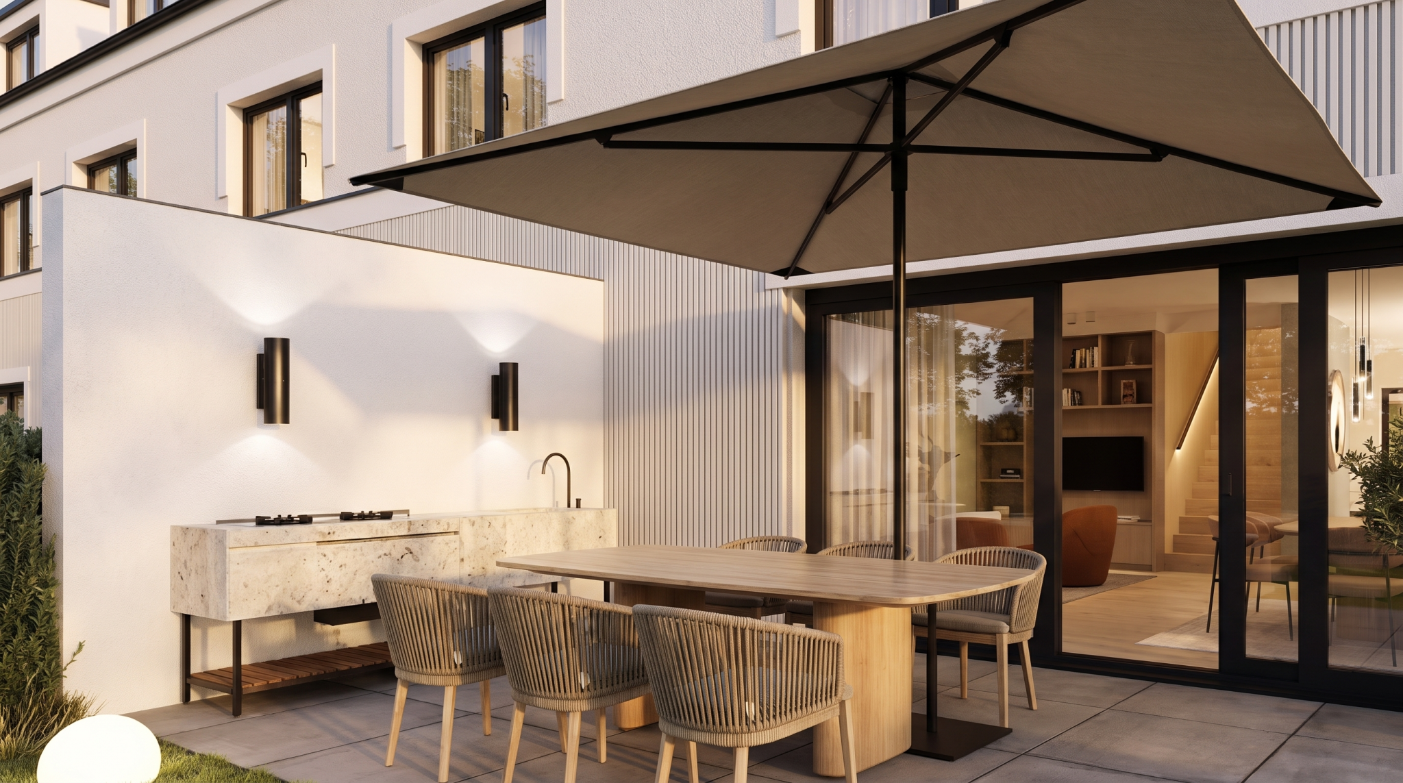 Terrasse mit Außenküche aus Naturstein, Teakholztisch unter Sonnenschirm und Schiebeglastüren abends, München Solln
