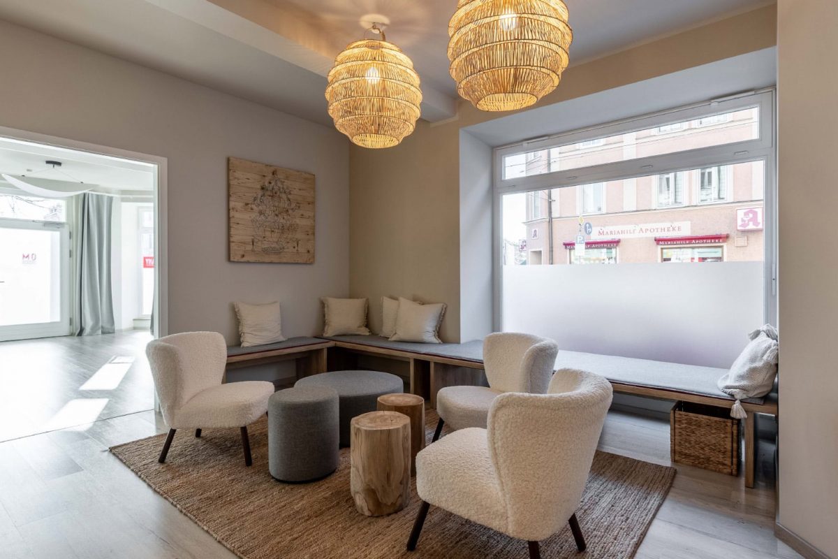 Innenarchitektur München / Innenarchitektur Federleicht - Lounge-Bereich im Yogastudio mit Holzmöbeln, weichen Stoffhockern und natürlicher Gestaltung