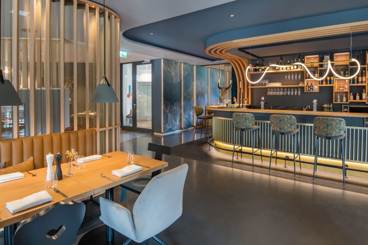 Innenarchitektur München / Innenarchitektur Federleicht - Offener Bar- und Speisebereich im La Soa Chalets mit geschwungenem Tresen, Holzlamellen und moderner Beleuchtung