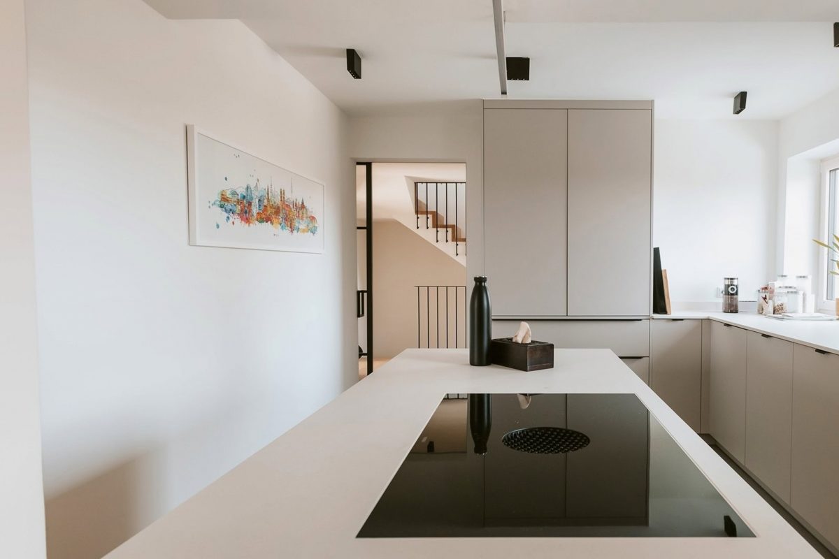 Innenarchitektur München, Büro Innenarchitektur Federleicht – Sanierung/Renovierung Reihenendhaus, moderne Küche mit Kochinsel, klaren Linien und Blick auf ein stilvolles Treppenhaus