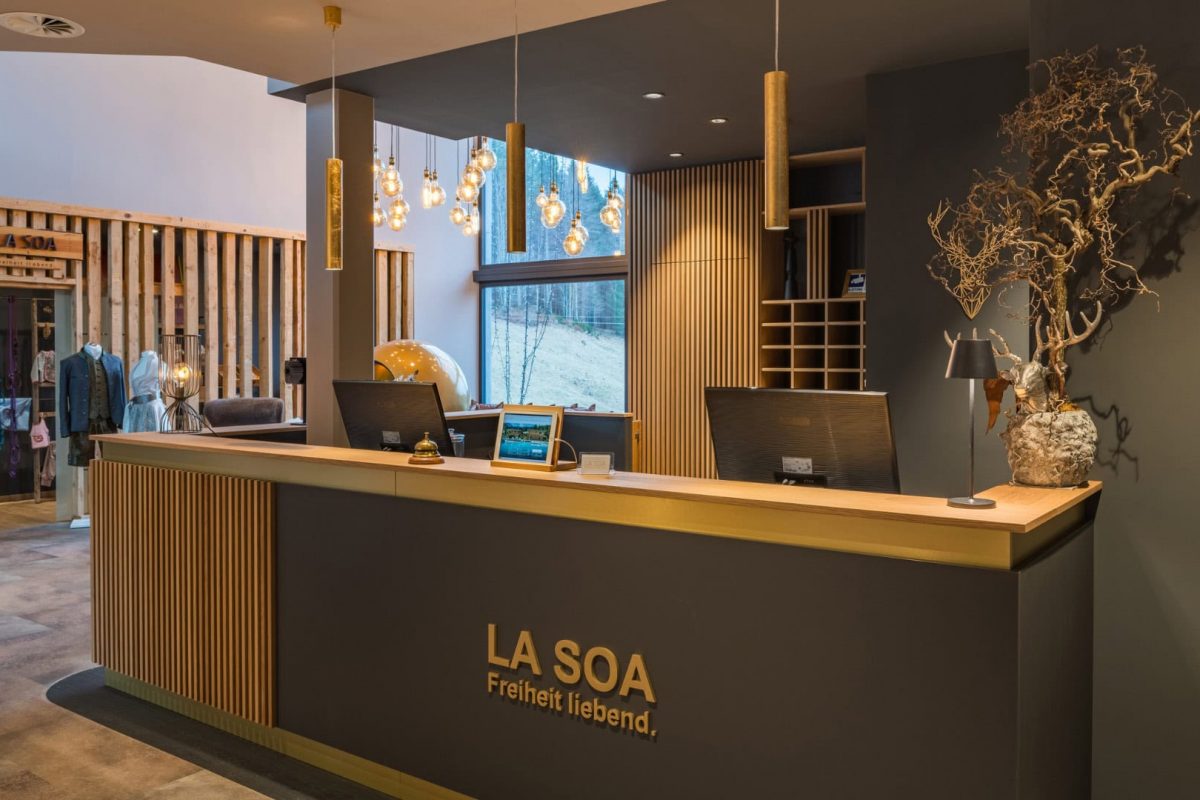 Innenarchitektur München / Innenarchitektur Federleicht - Empfangsbereich La Soa Chalets mit modernem Tresen, Holzlamellen und Messingakzenten