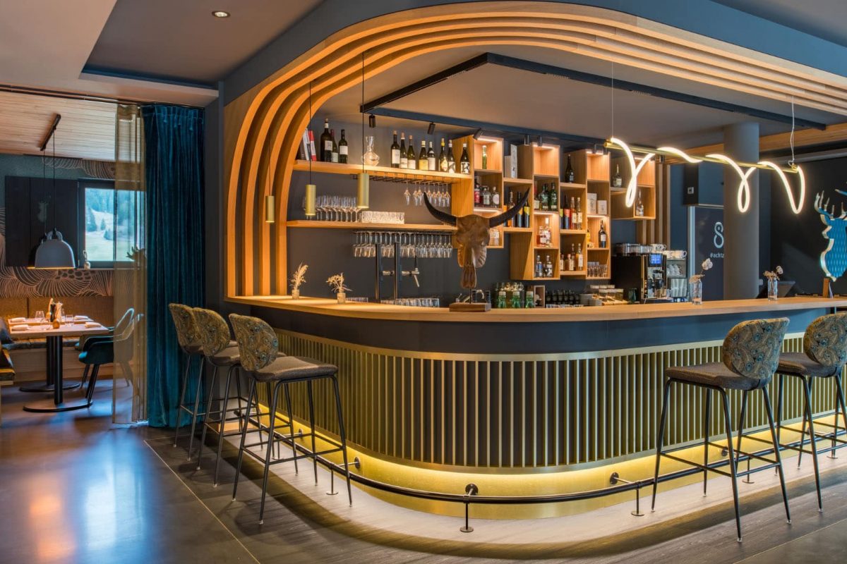 Innenarchitektur München / Innenarchitektur Federleicht - Barbereich La Soa Chalets mit geschwungenem Tresen, Holzdetails und Messingakzenten im modernen alpinen Stil